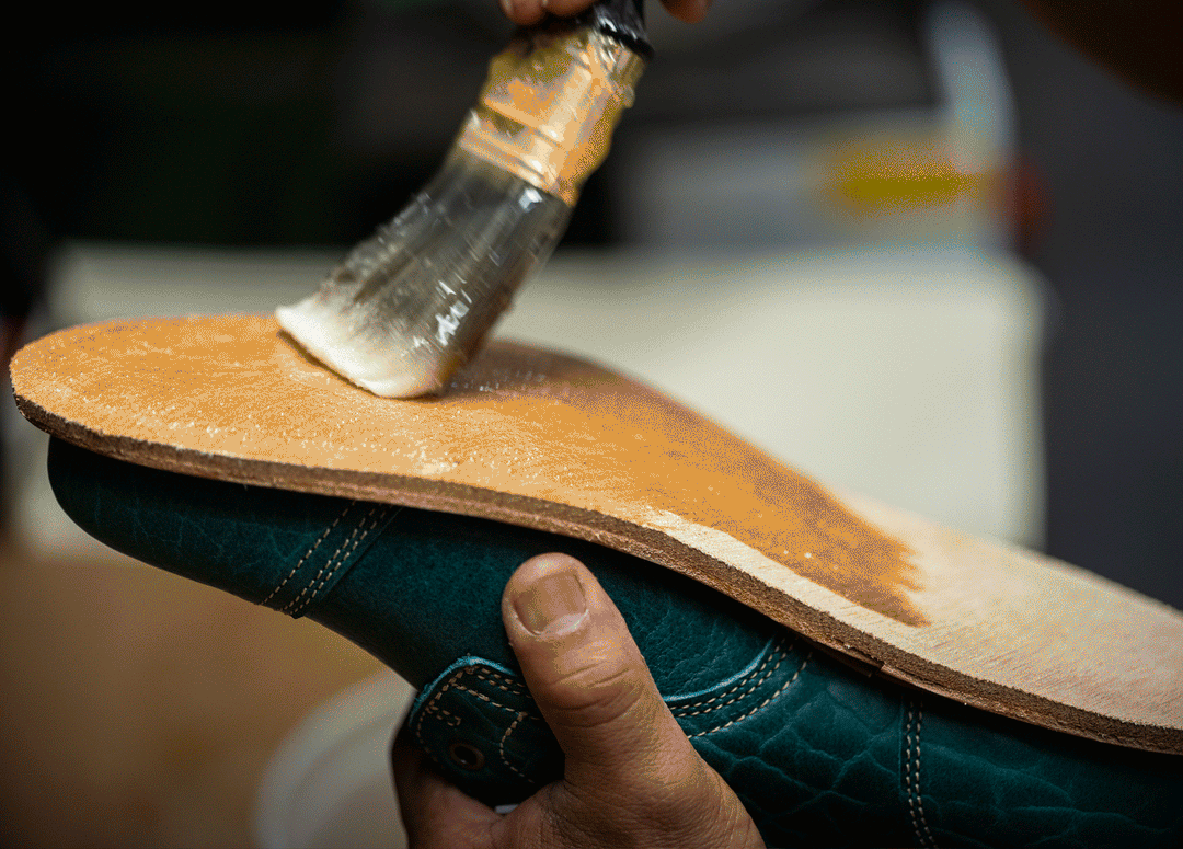 hand using brush to apply adhesive to bottom of midsole of boot