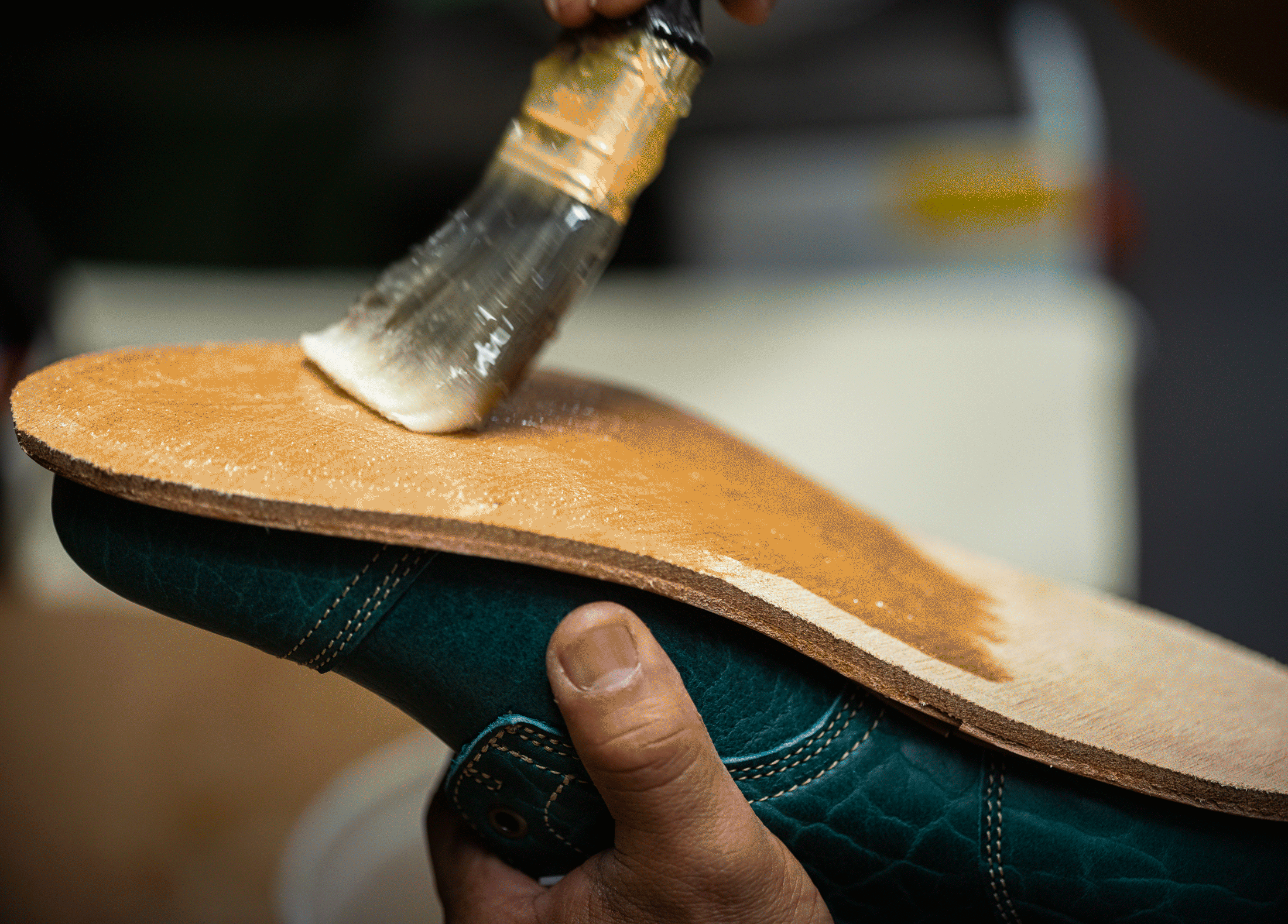 hand using brush to apply adhesive to bottom of midsole of boot