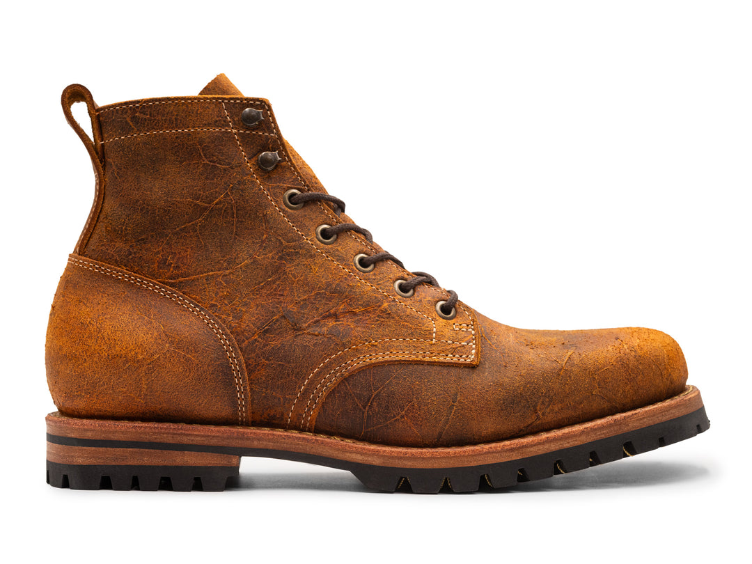 side view of brown orange textured leather boot on white background