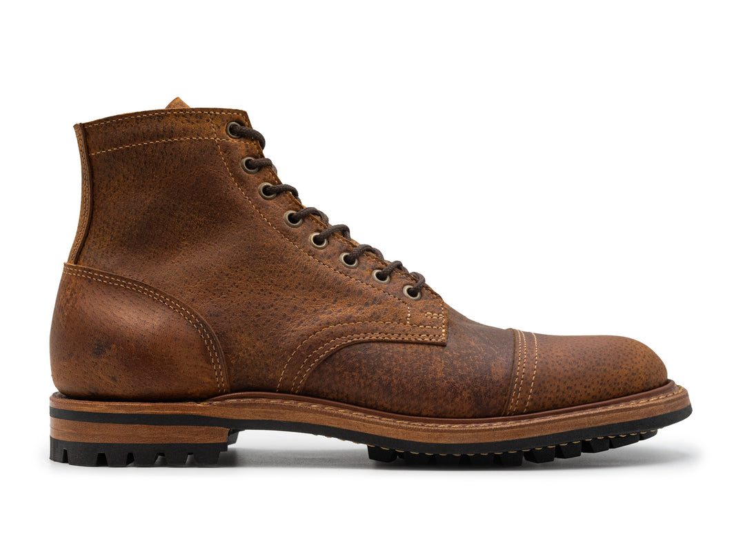 side view of textured brown leather cap toe boot on white background