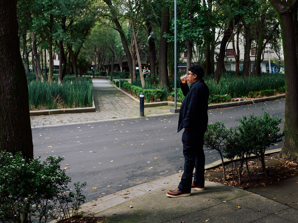 man standing in brown leather moc toe boots near street with greenery in background