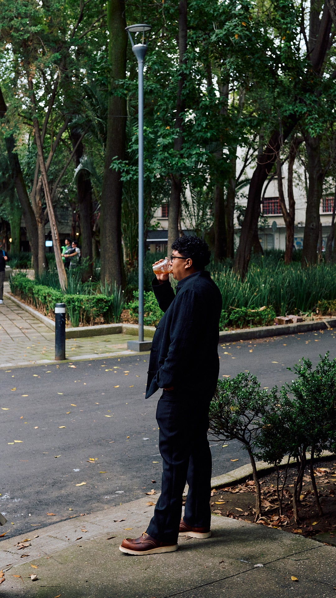 man standing in brown leather moc toe boots near street with greenery in background