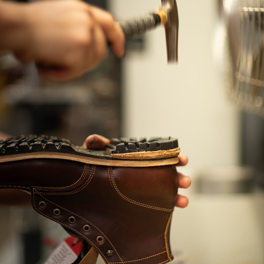 hand in motion swinging hammer to nail heels on brown leather moc toe boot