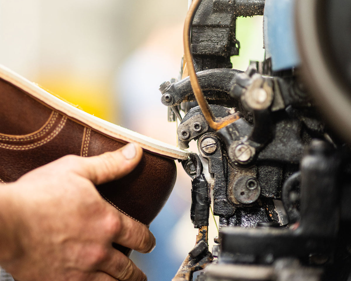close up shot of hand guiding boot along outsole stitcher