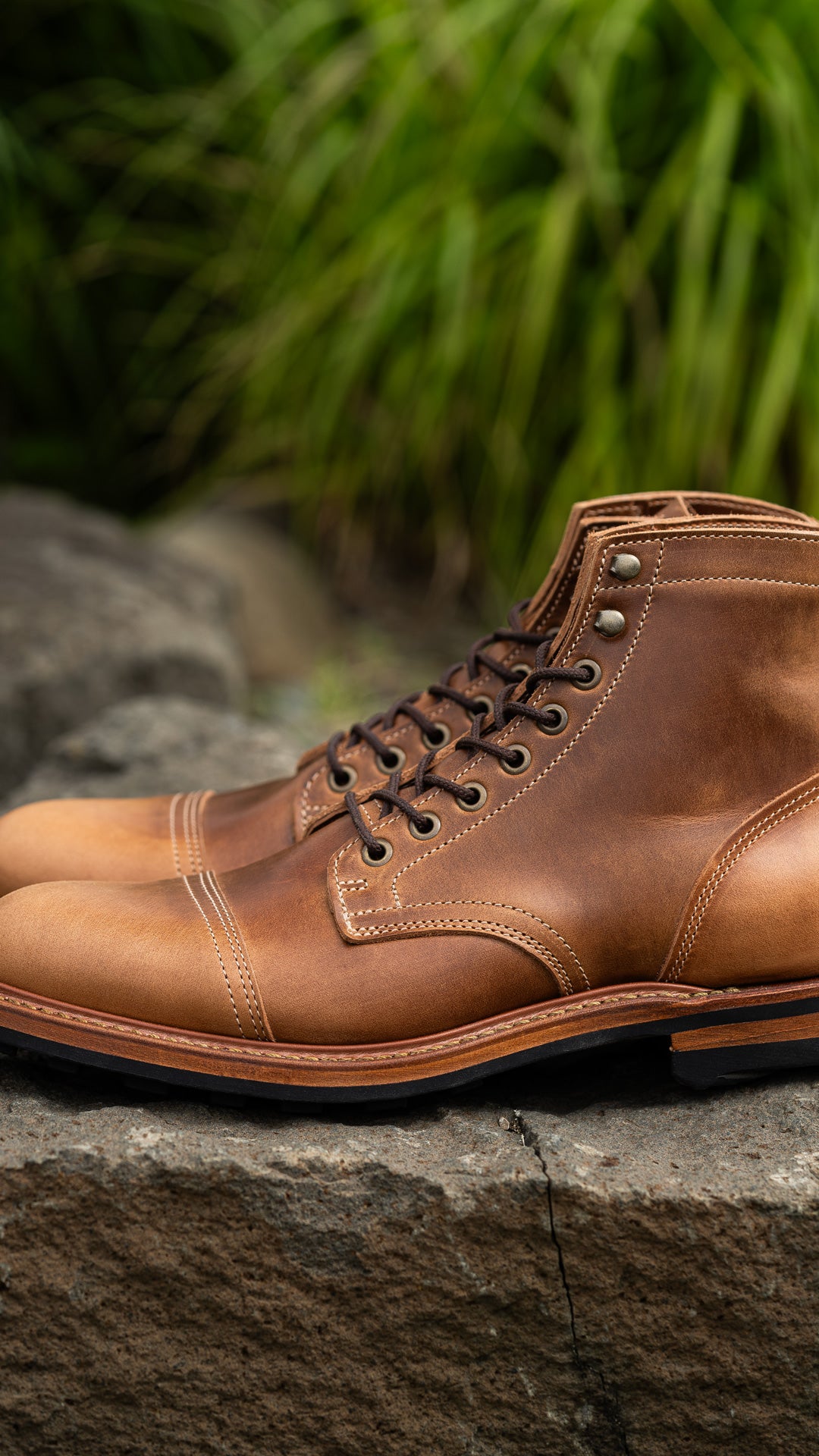 pair of caramel tan boots sitting on stone with green in background
