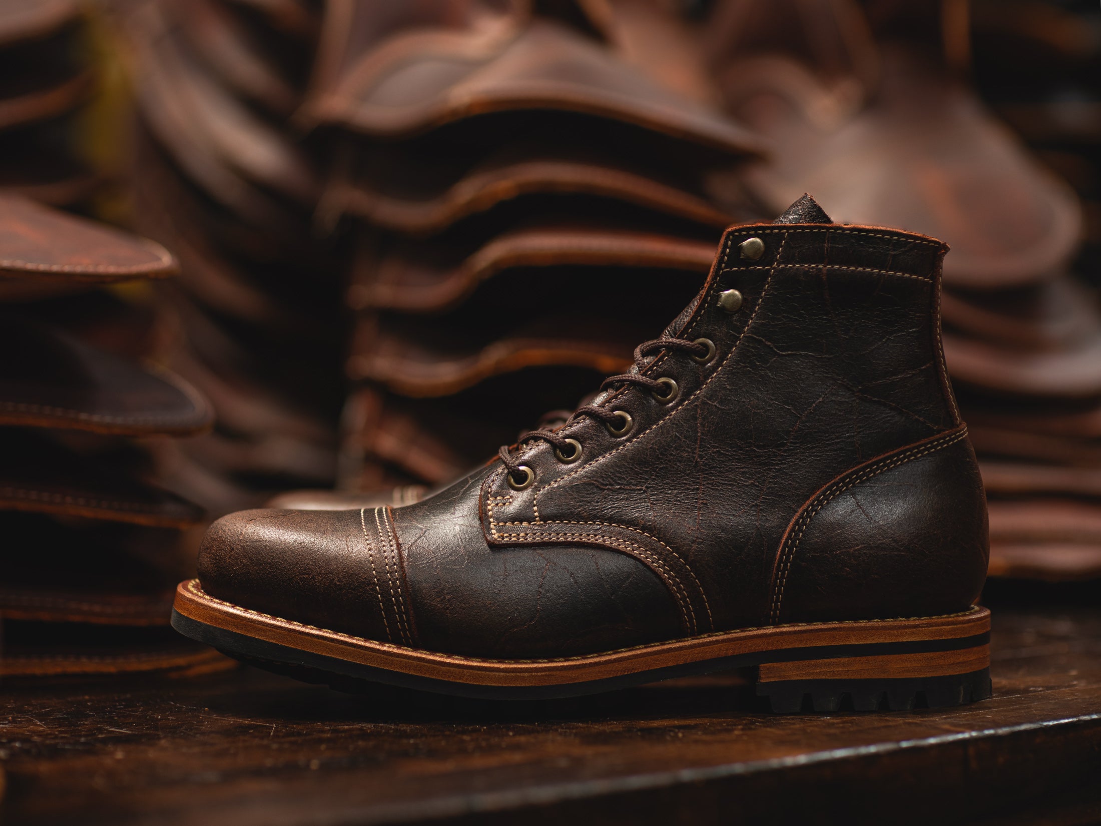 textured brown leather boot on dark wood table with leather behind