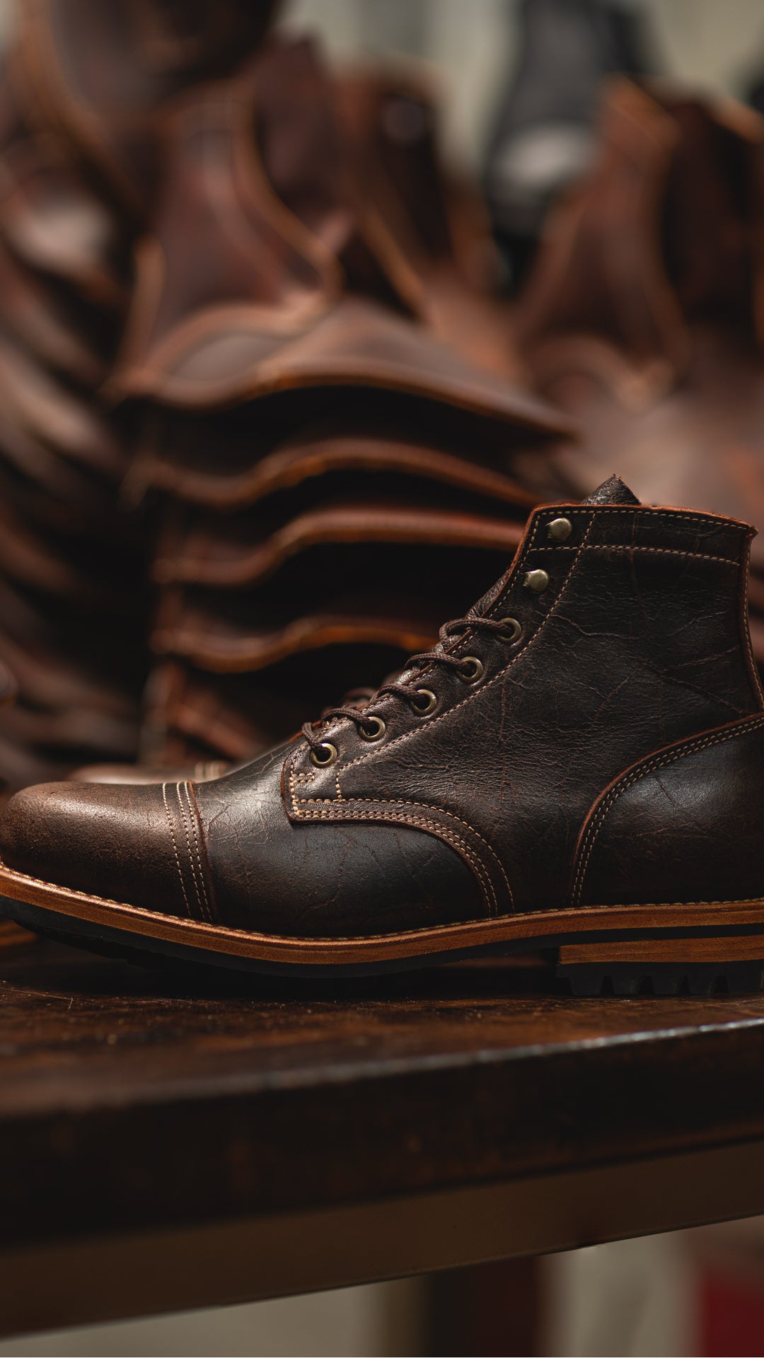 textured brown leather boot on dark wood table with leather behind