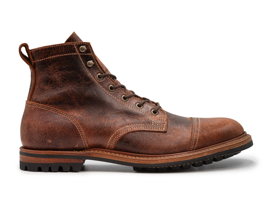 side view of reddish brown textured leather boot on white background
